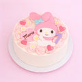 A round white cake decorated with pink frosting rosettes, small daisy flowers, pink hearts, and a large pink character topper resembling My Melody, with the name 'Maria' on a pink heart and a purple number 7, set on a white plate against a pink background.